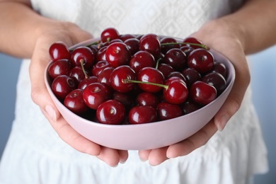 Woman holding bowl with ripe cherries, closeup