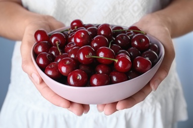 Photo of Woman holding bowl with ripe cherries, closeup