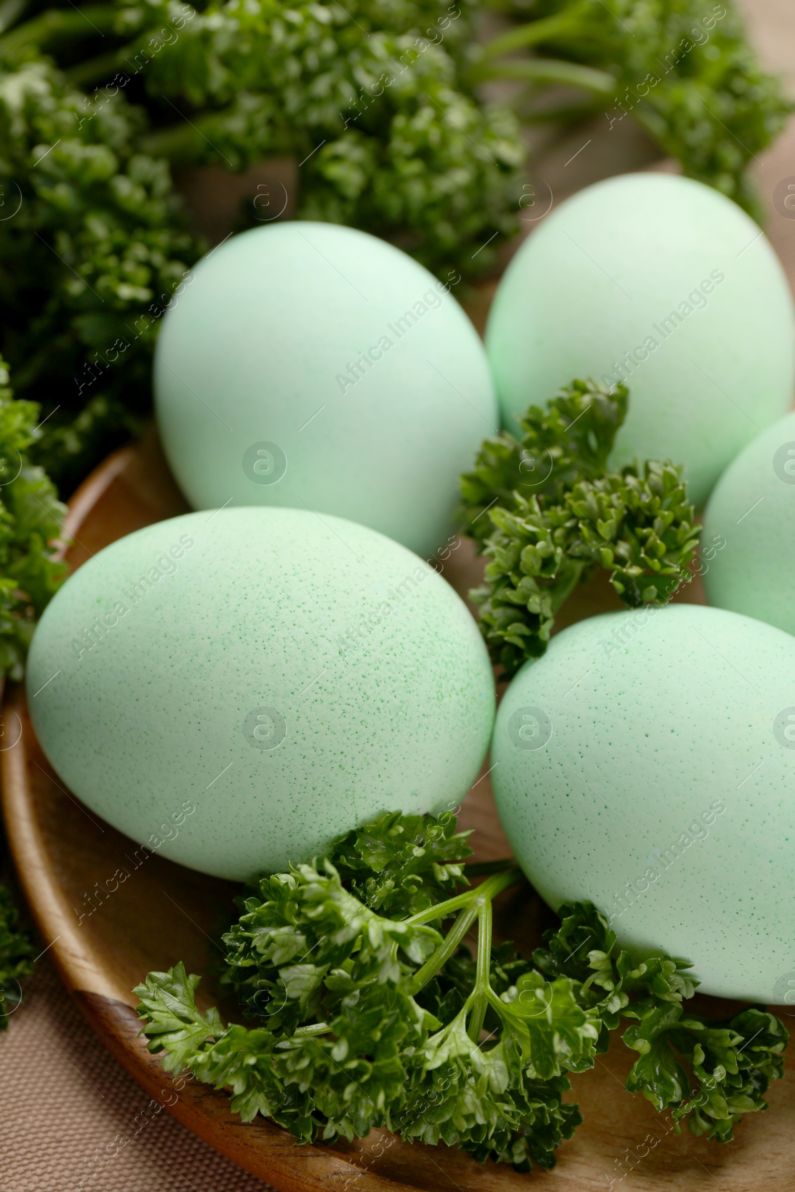 Photo of Turquoise Easter eggs painted with natural dye and curly parsley on table, closeup