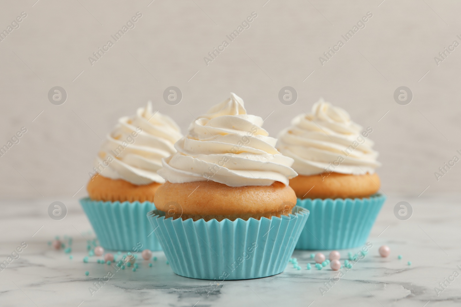 Photo of Delicious cupcakes decorated with cream on white marble table