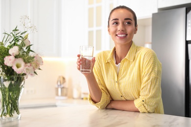 Young woman holding glass of pure water in kitchen