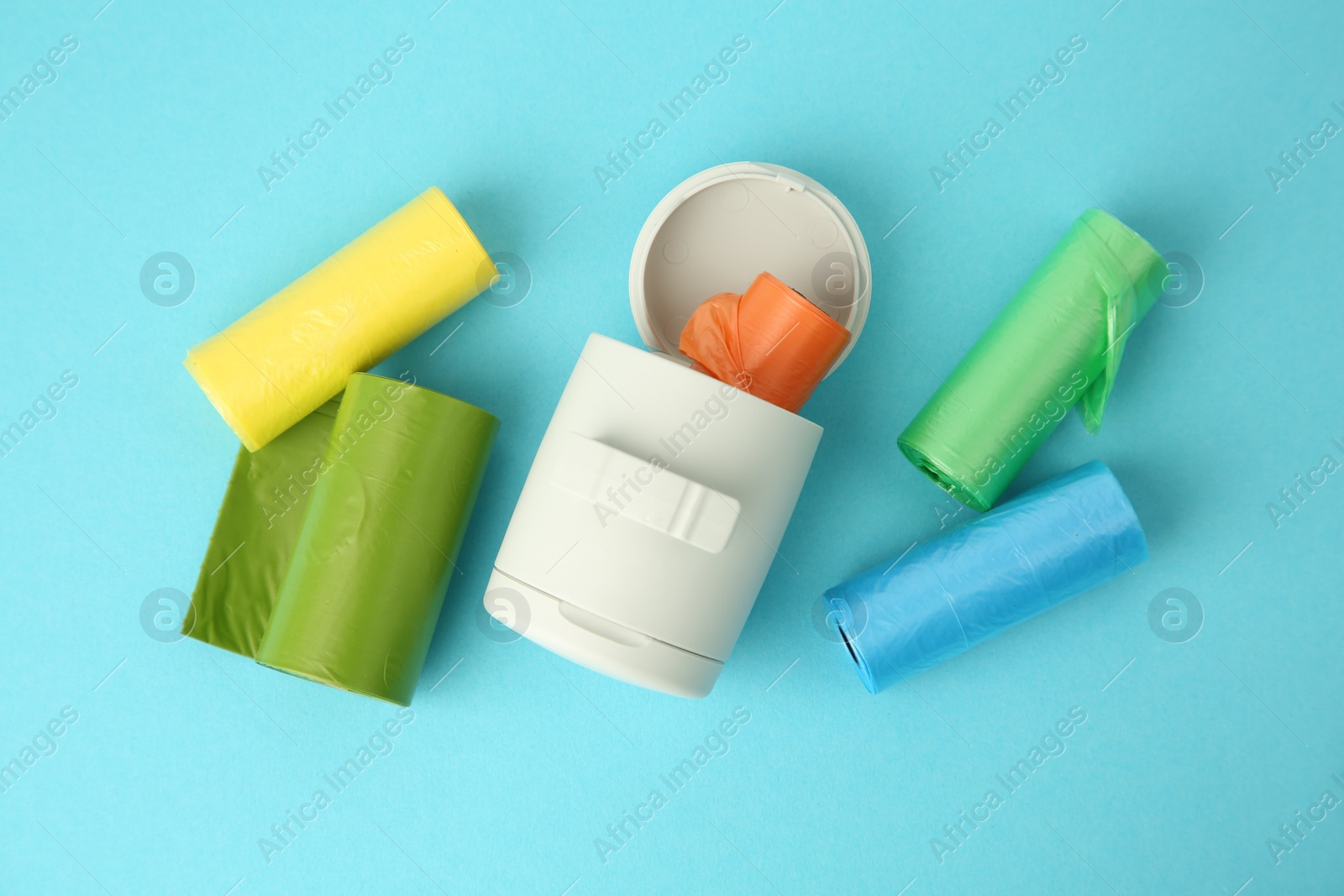 Photo of Dog waste bags and dispenser on light blue background, flat lay