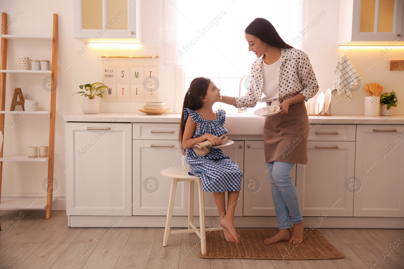 Photo of Mother and daughter wiping dishes together in kitchen