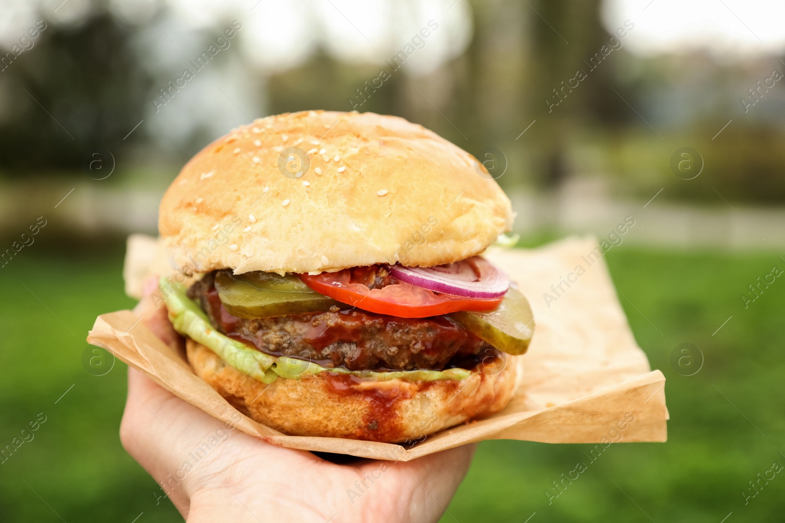 Photo of Little girl holding fresh delicious burger outdoors, closeup. Street food