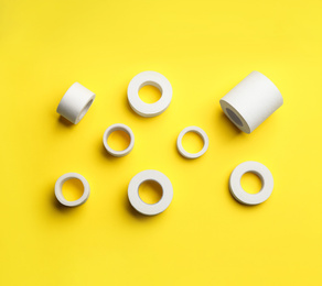 Photo of Sticking plaster rolls on yellow background, flat lay