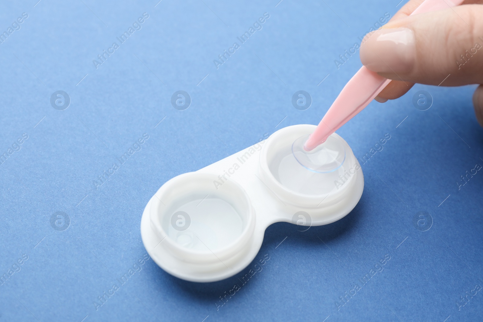 Photo of Woman taking contact lens from case with tweezers on blue background, closeup