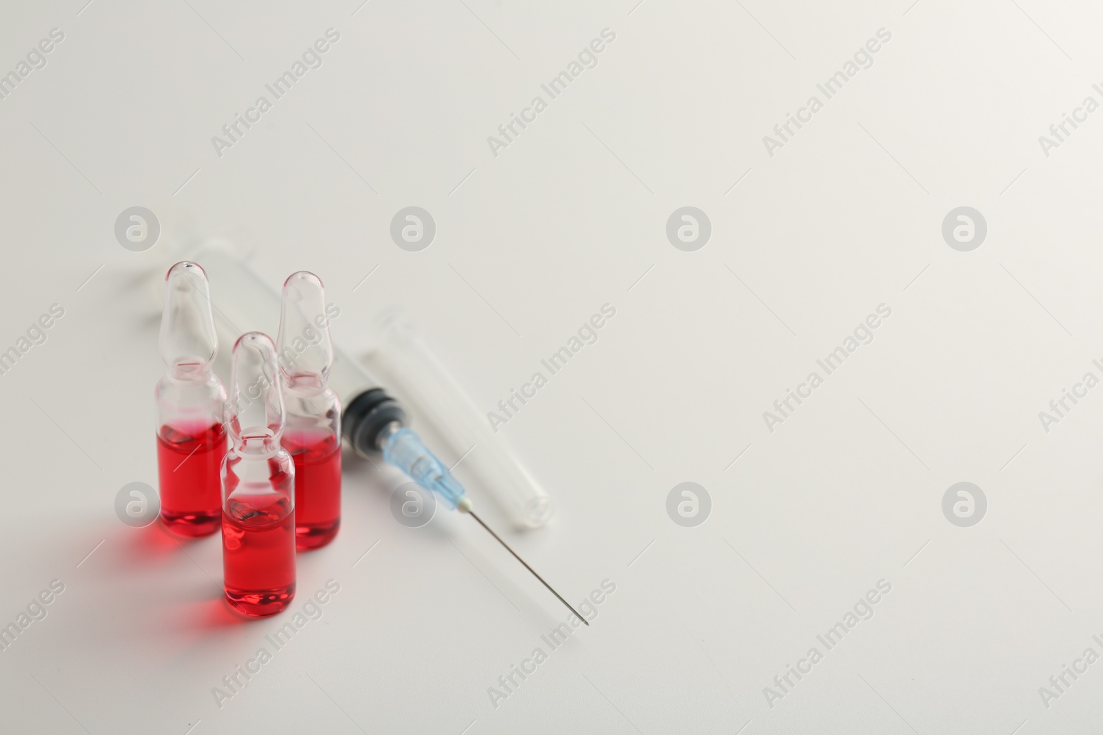 Photo of Glass ampoules with liquid and syringe on white background, closeup. Space for text