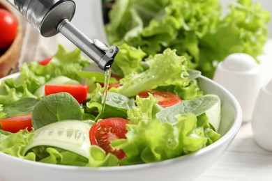 Photo of Pouring oil into delicious vegetable salad on white table, closeup