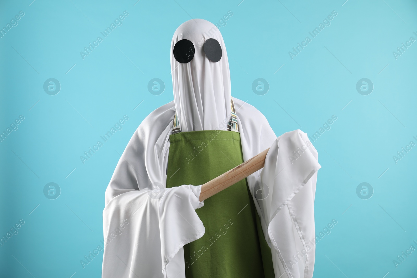 Photo of Woman in ghost costume and apron with rolling pin on light blue background