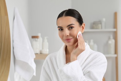 Photo of Beautiful woman removing makeup with cotton pad in bathroom, space for text