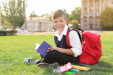 Schoolboy with stationery sitting on grass outdoors