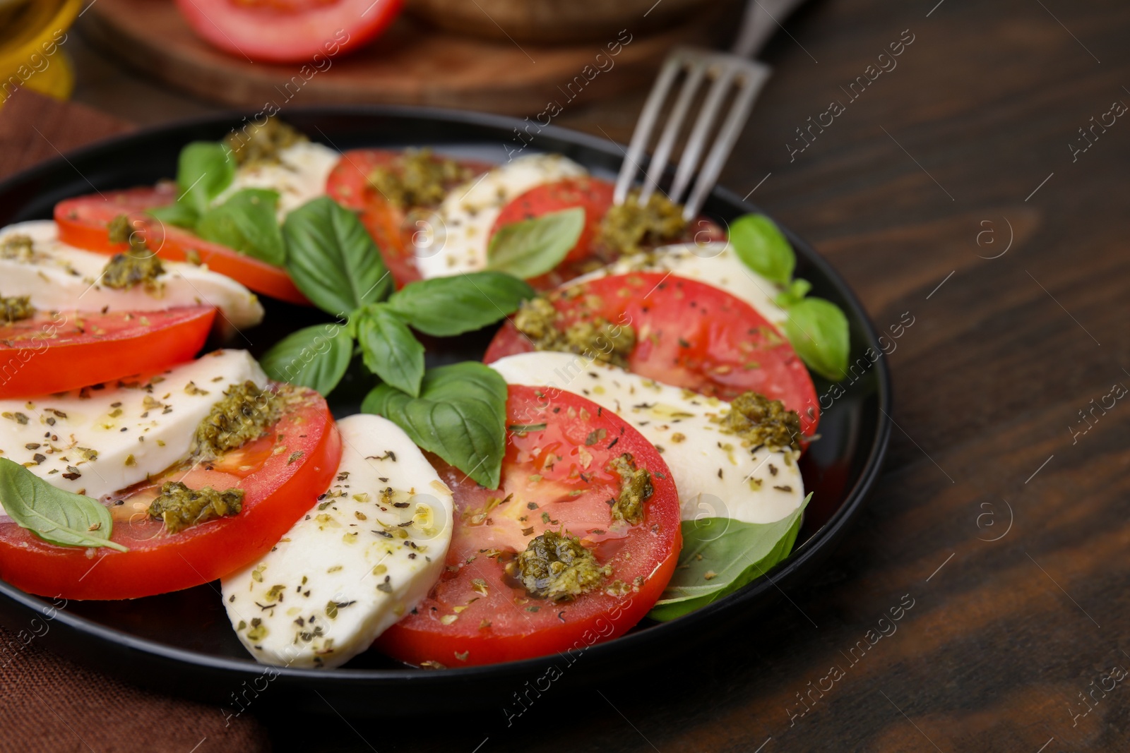 Photo of Plate of delicious Caprese salad with pesto sauce on wooden table, closeup. Space for text