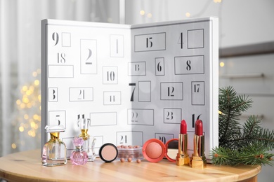 Photo of Advent calendar with different cosmetics and perfumes on wooden table against blurred lights. Presents for Christmas