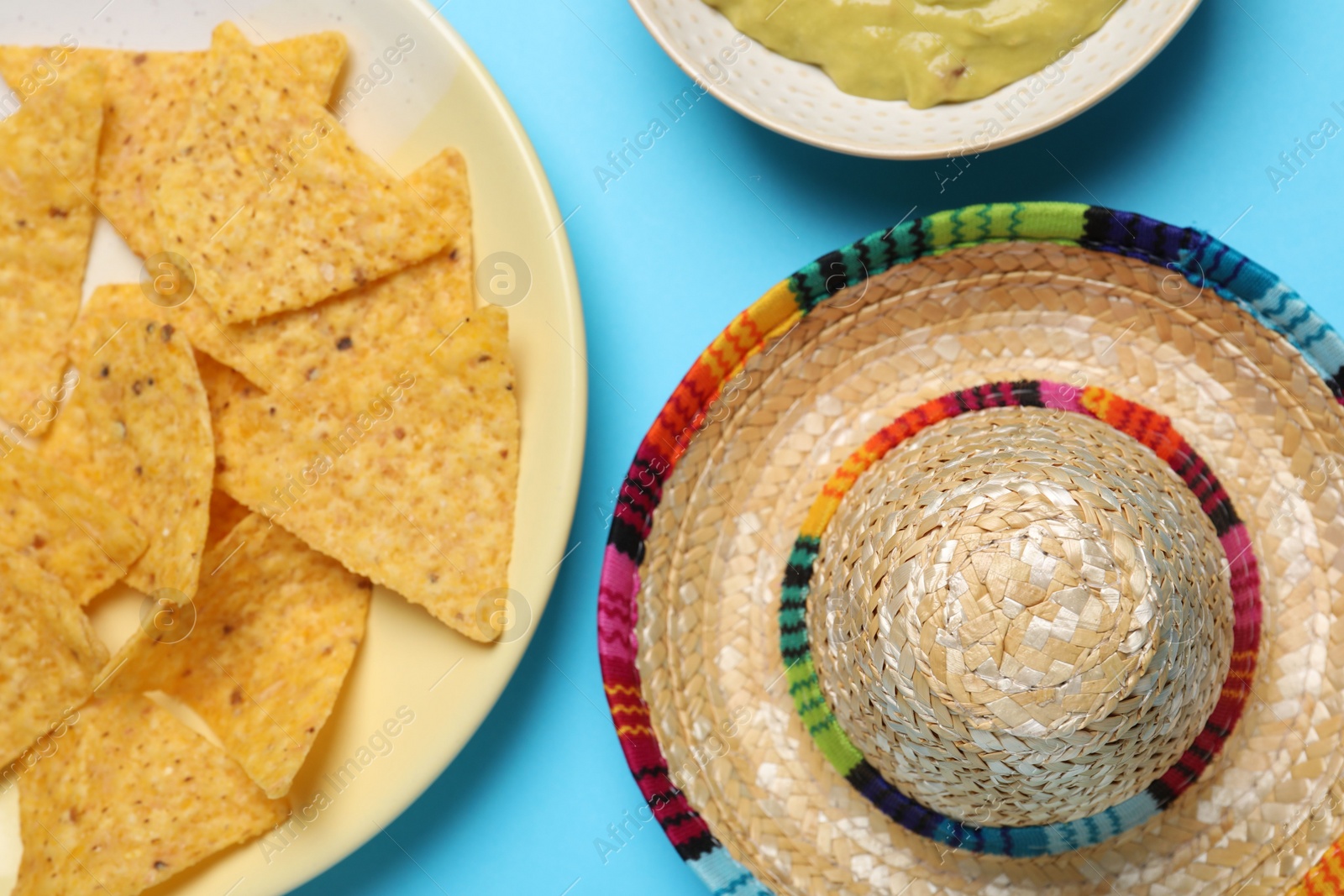 Photo of Mexican sombrero hat and nachos chips on light blue background, top view