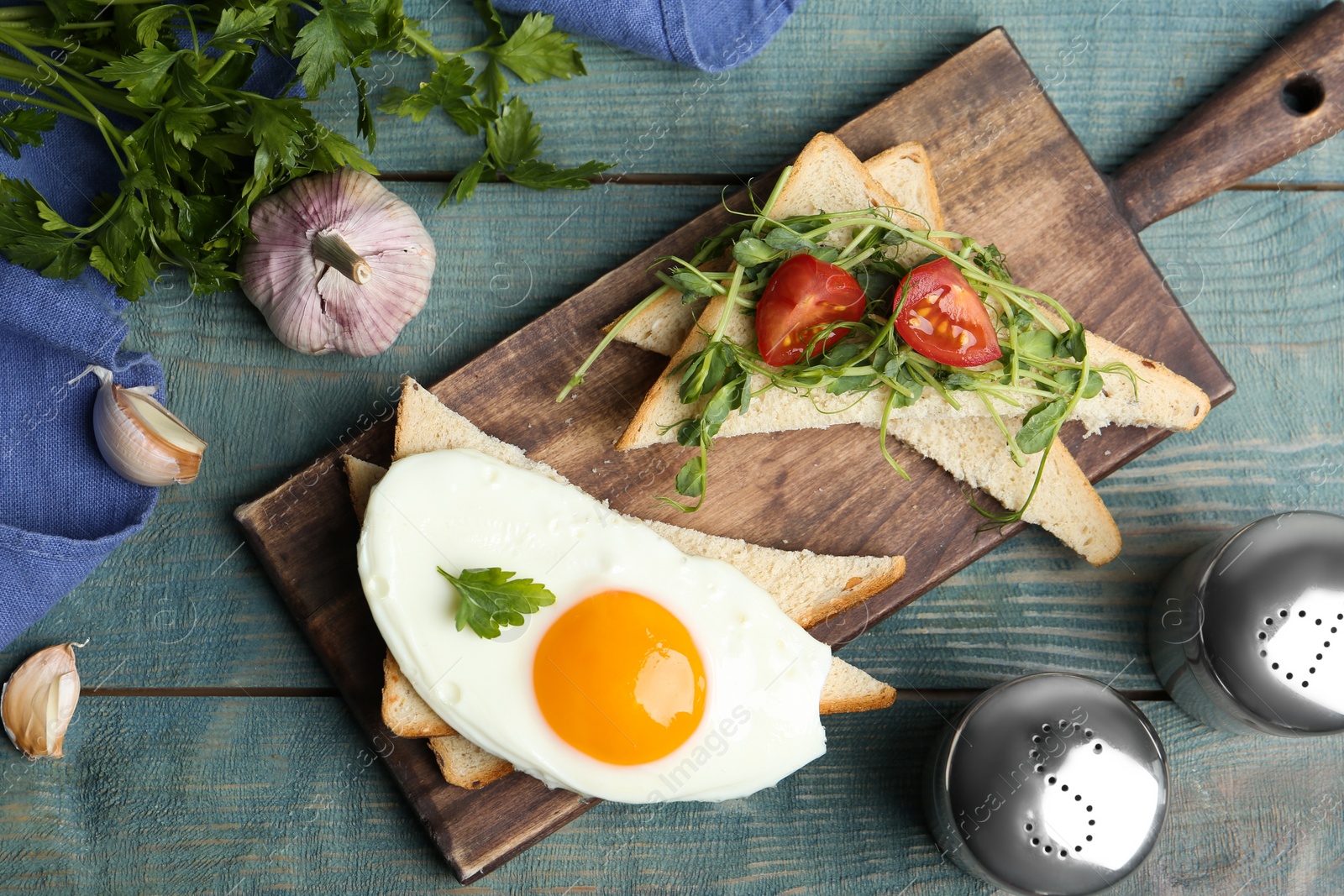 Photo of Tasty fried egg with bread, tomato and sprouts on blue wooden table, flat lay