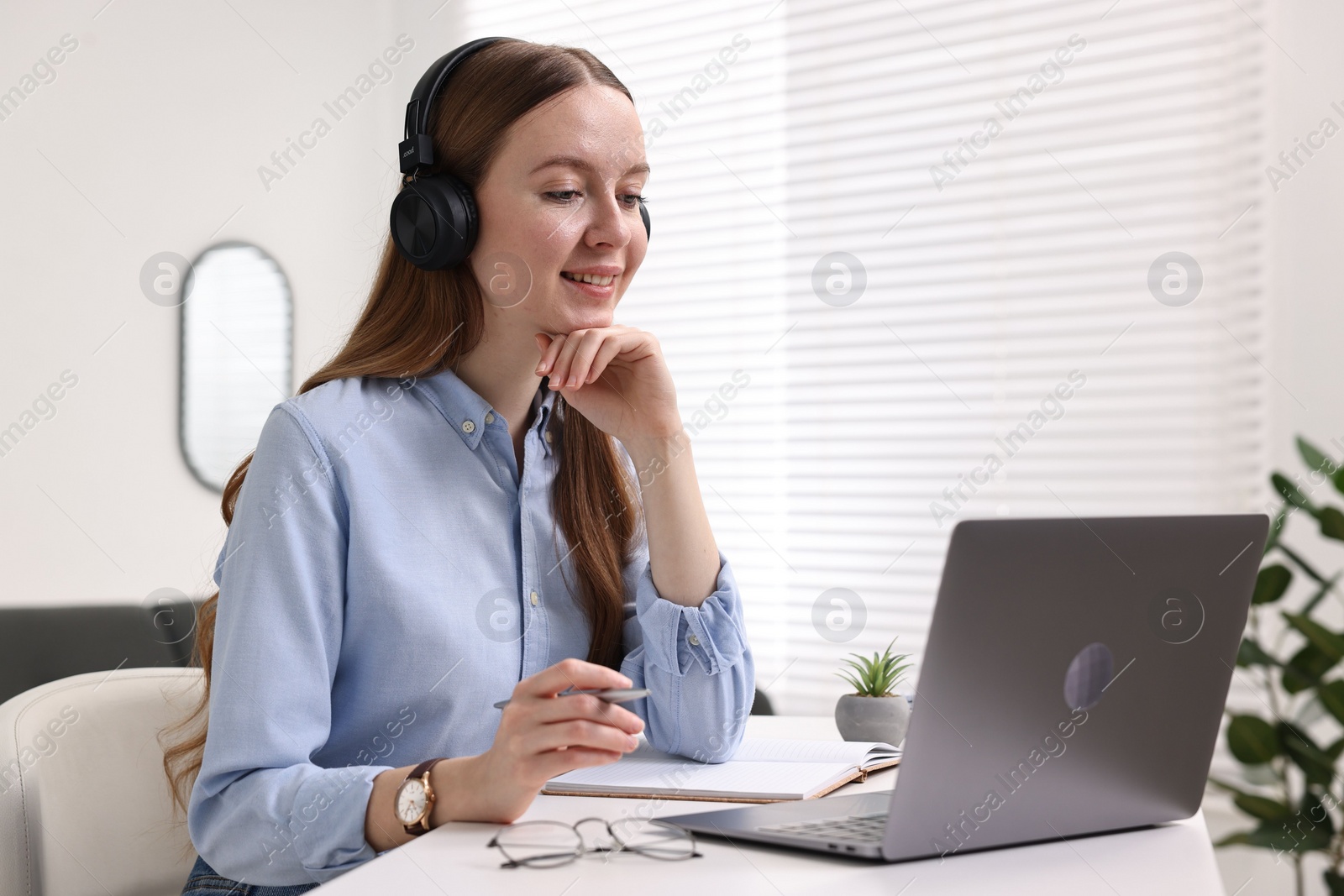 Photo of E-learning. Young woman using laptop during online lesson at white table indoors