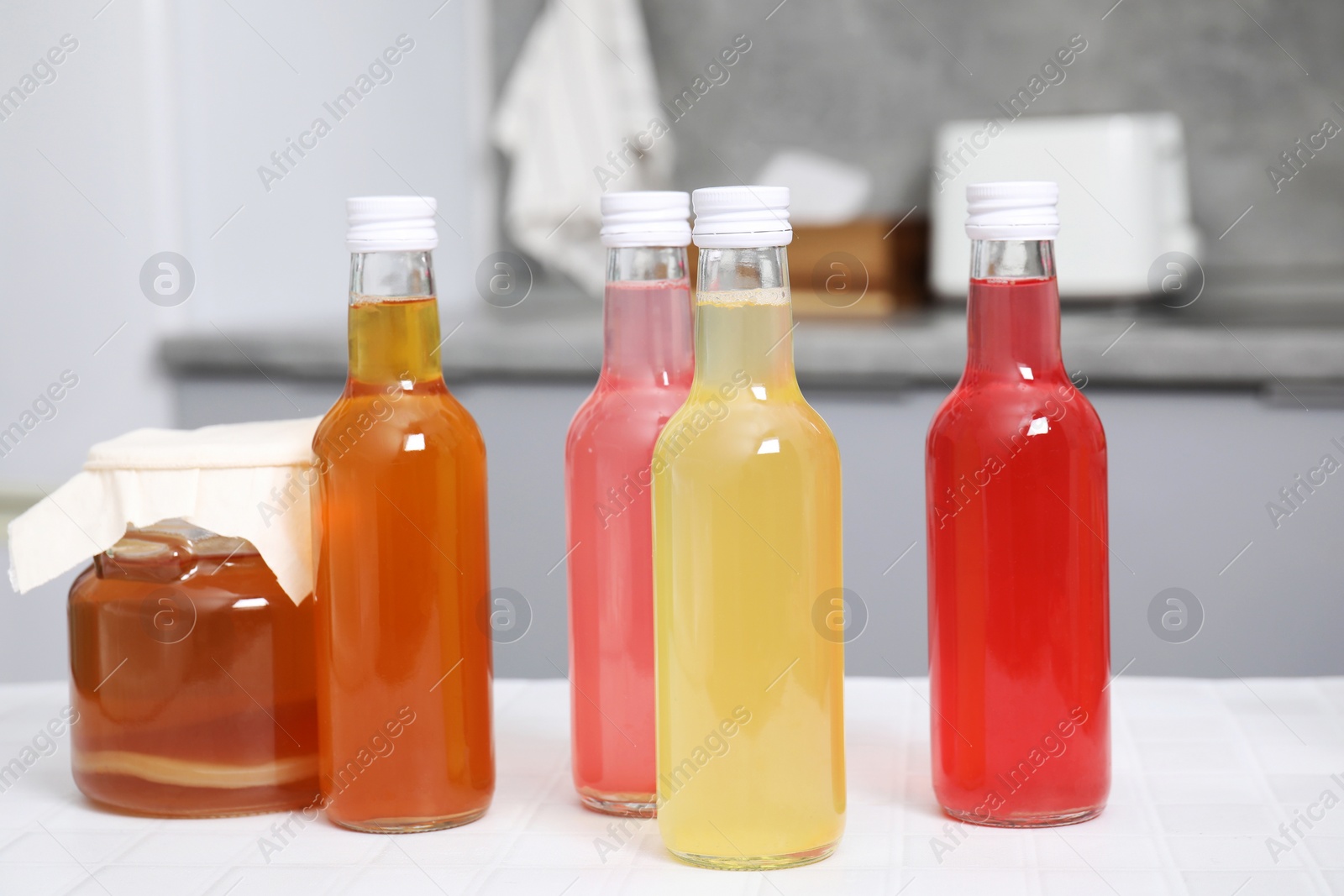 Photo of Tasty kombucha in glass bottles and jar on white tiled table