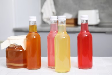 Tasty kombucha in glass bottles and jar on white tiled table