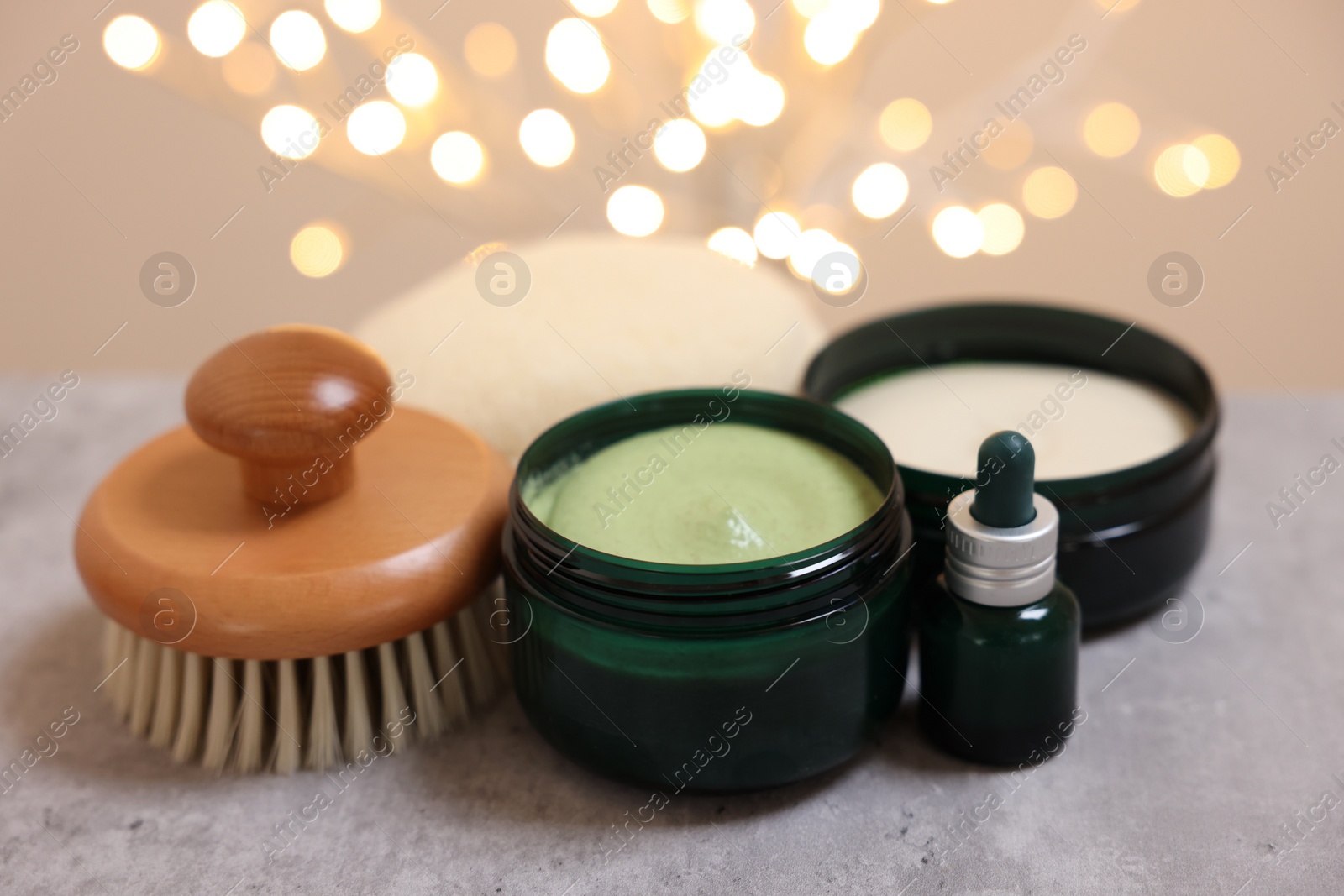 Photo of Natural scrub and other body care products on grey table against blurred lights