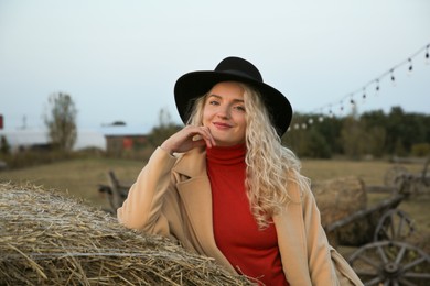 Photo of Beautiful woman sitting near hay bales outdoors. Autumn season