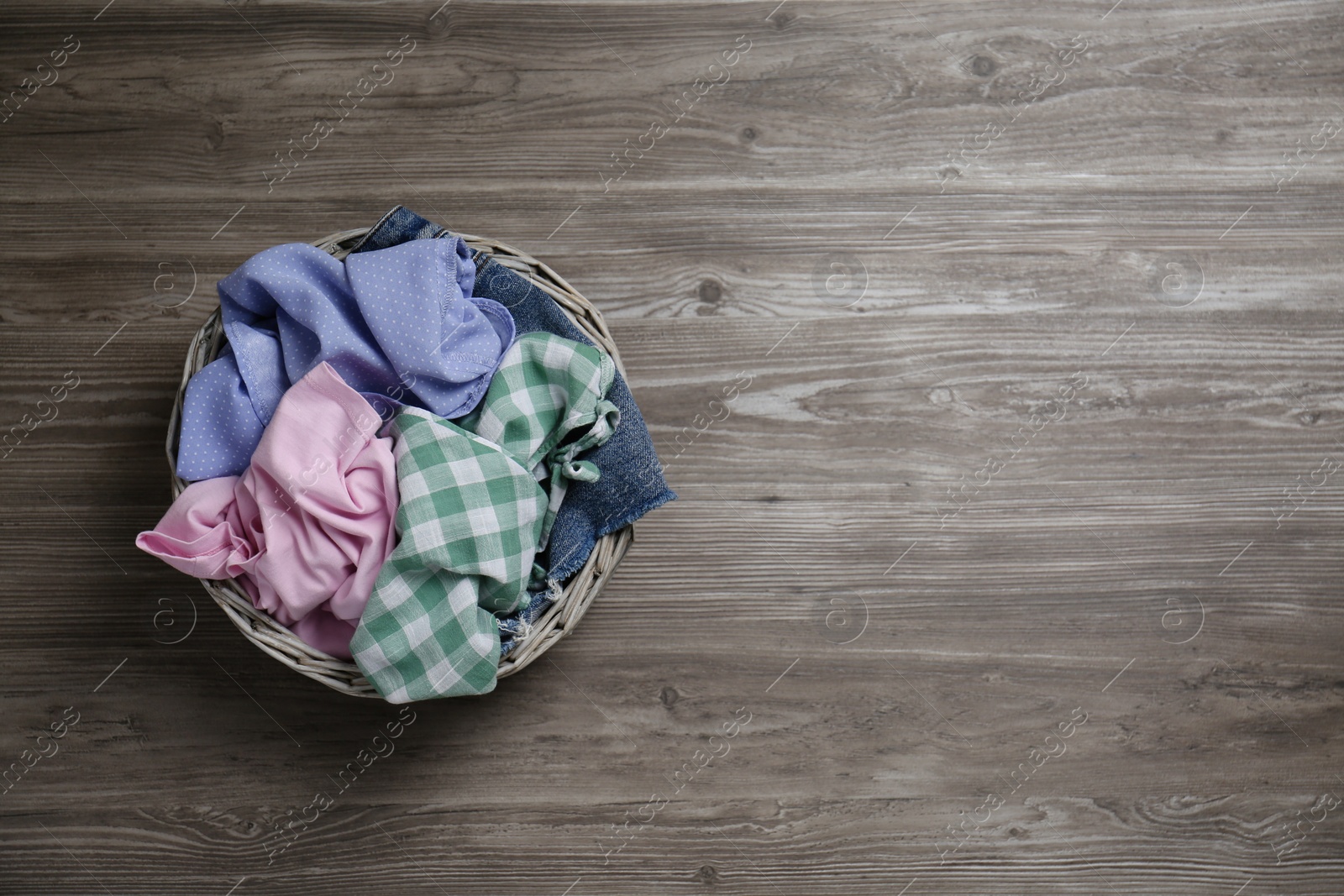 Photo of Wicker laundry basket with different clothes on wooden background, top view. Space for text