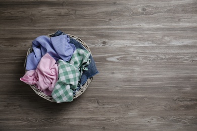 Photo of Wicker laundry basket with different clothes on wooden background, top view. Space for text