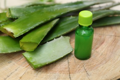 Photo of Fresh aloe vera leaves and bottle of extract on wooden stump