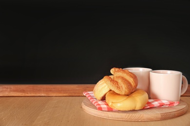 Photo of Cups and baked goods on wooden table near chalkboard