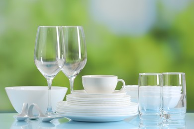 Photo of Set of many clean dishware and glasses on light blue table against blurred green background
