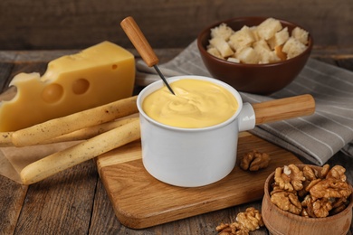 Photo of Pot of tasty cheese fondue and products on wooden table