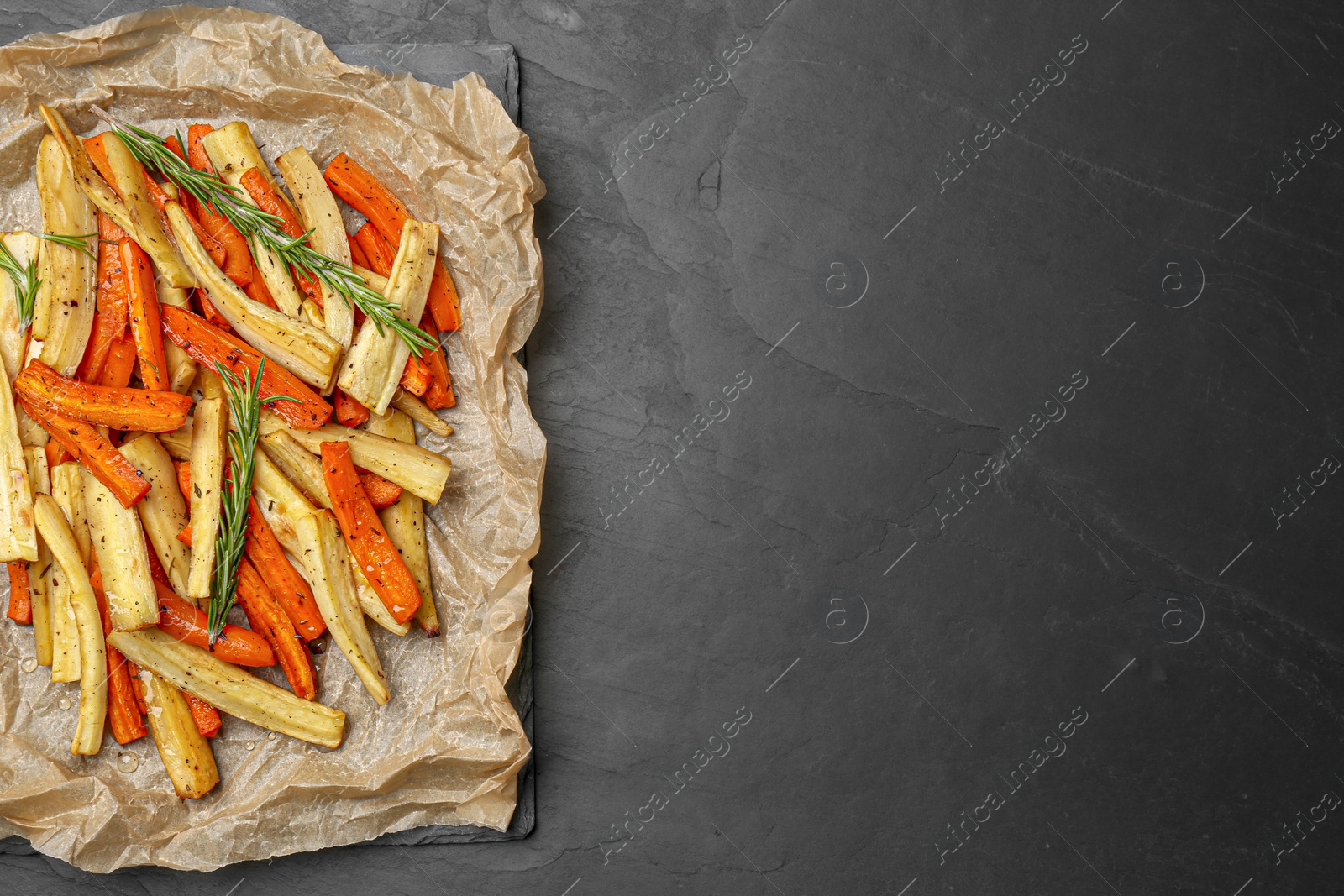 Photo of Parchment with tasty baked parsnip and bell pepper on dark grey table, top view. Space for text