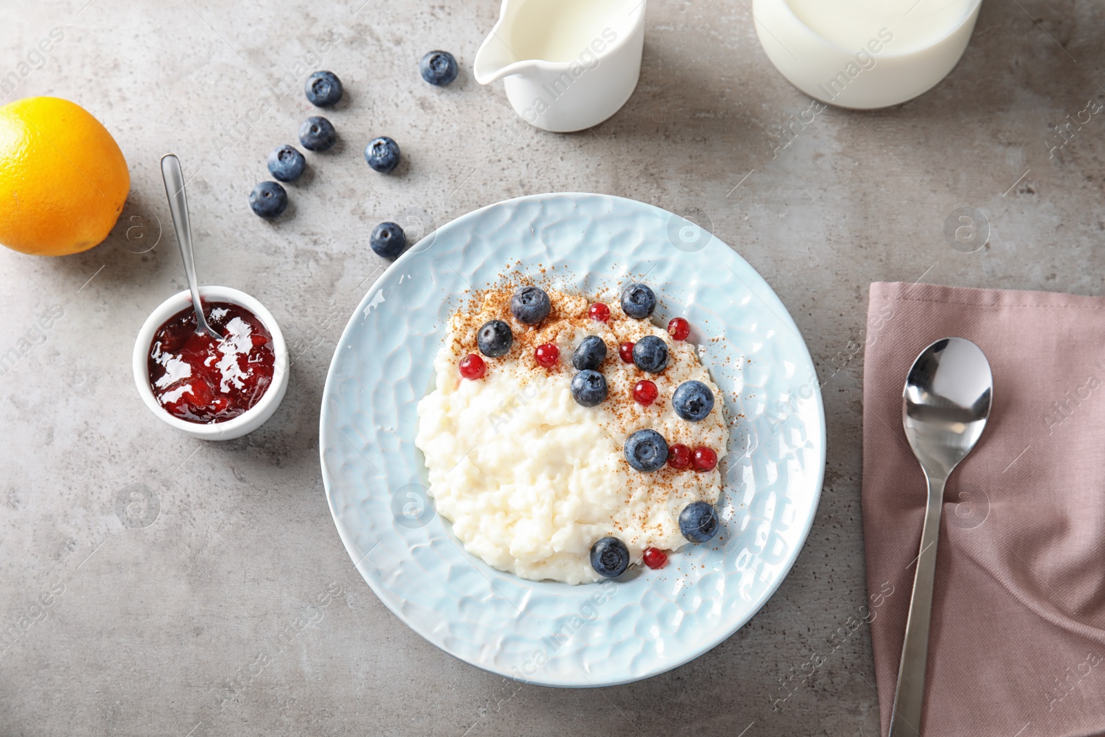 Photo of Creamy rice pudding with red currant and blueberries in bowl served on grey table, top view