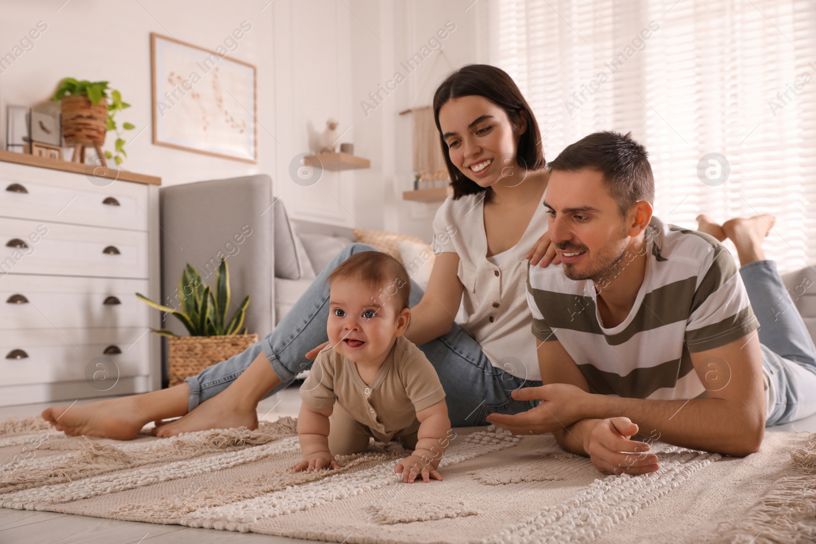 Photo of Happy parents watching their cute baby crawl on floor at home