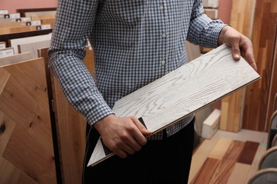 Man with sample of light wooden flooring in shop, closeup