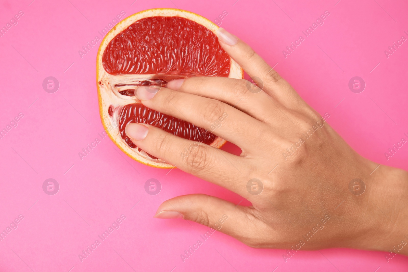 Photo of Young woman touching half of grapefruit on pink background, top view. Sex concept