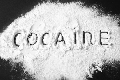 Heap of white powder with written word Cocaine on black background, top view