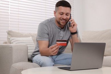 Handsome man with credit card using smartphone for online shopping at home