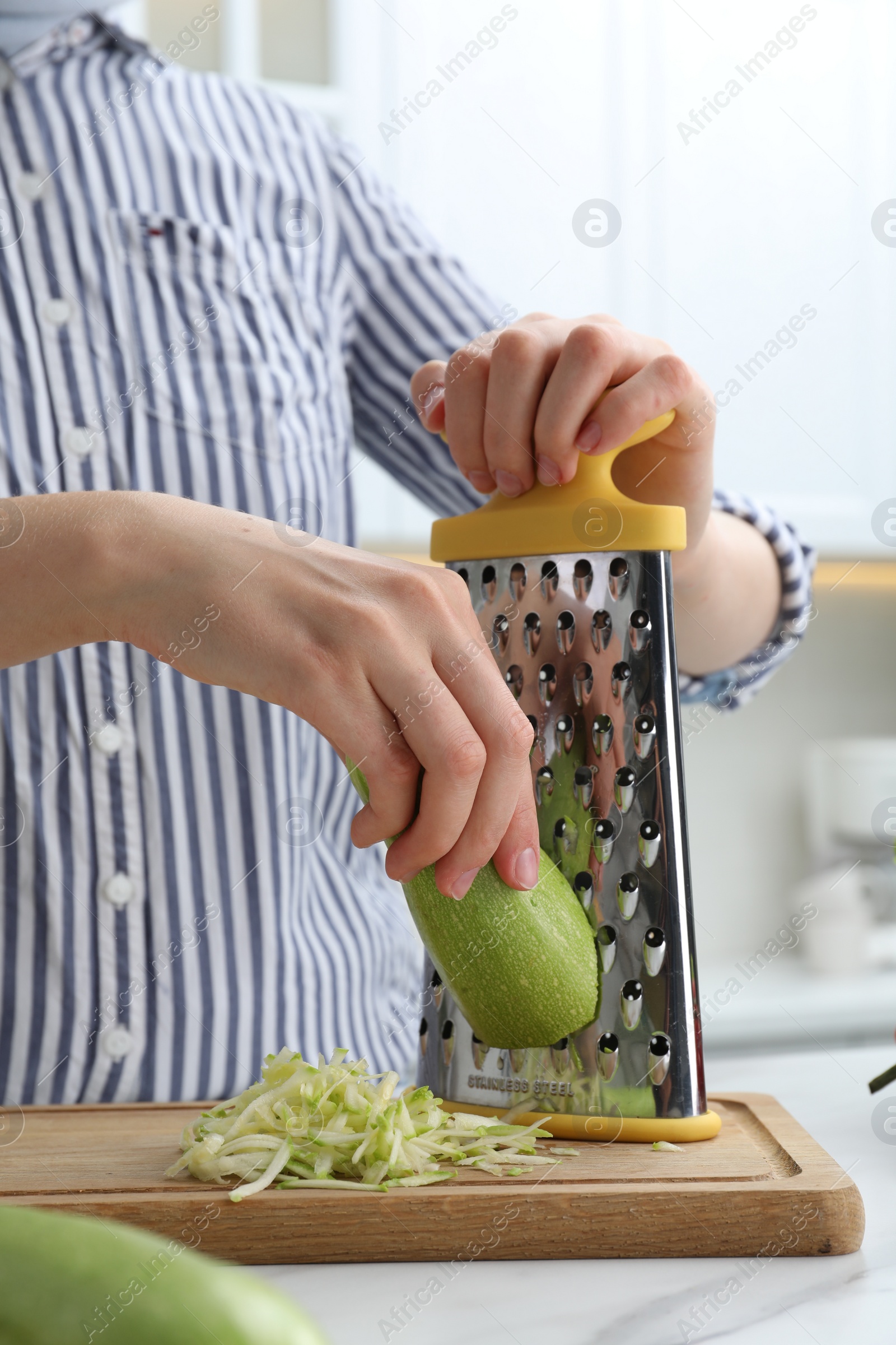 Photo of Woman grating zucchini at kitchen table, closeup