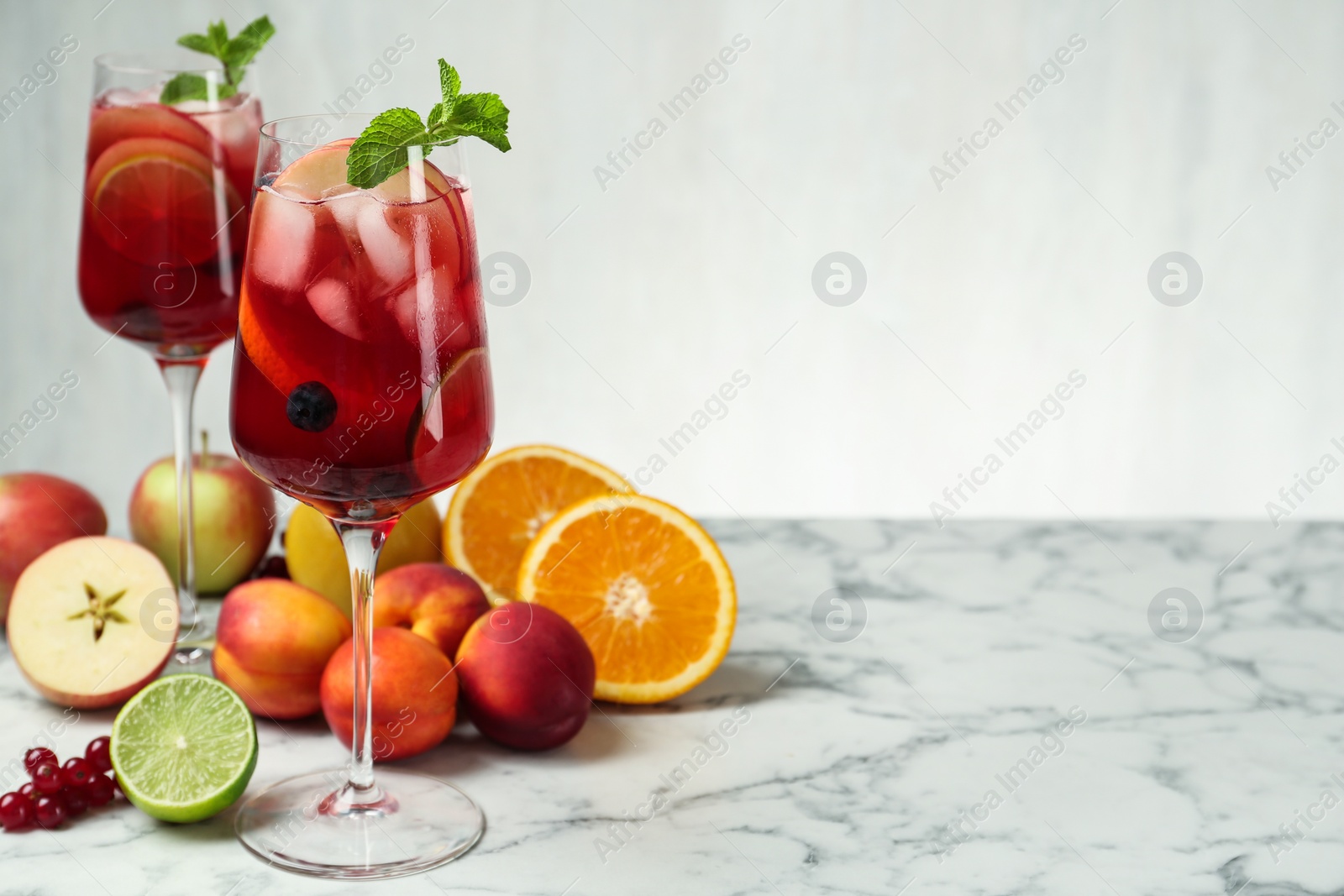 Photo of Delicious Red Sangria and fruits on white marble table, space for text