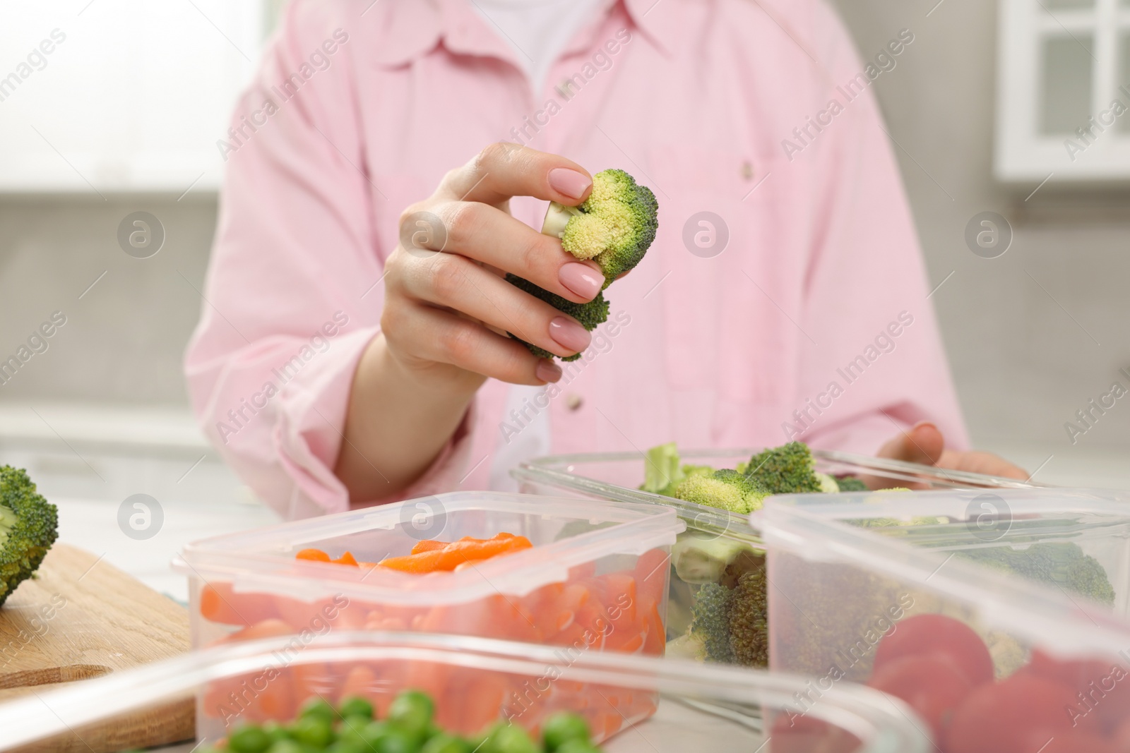 Photo of Woman putting green broccoli into glass container in kitchen, closeup