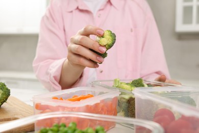 Woman putting green broccoli into glass container in kitchen, closeup