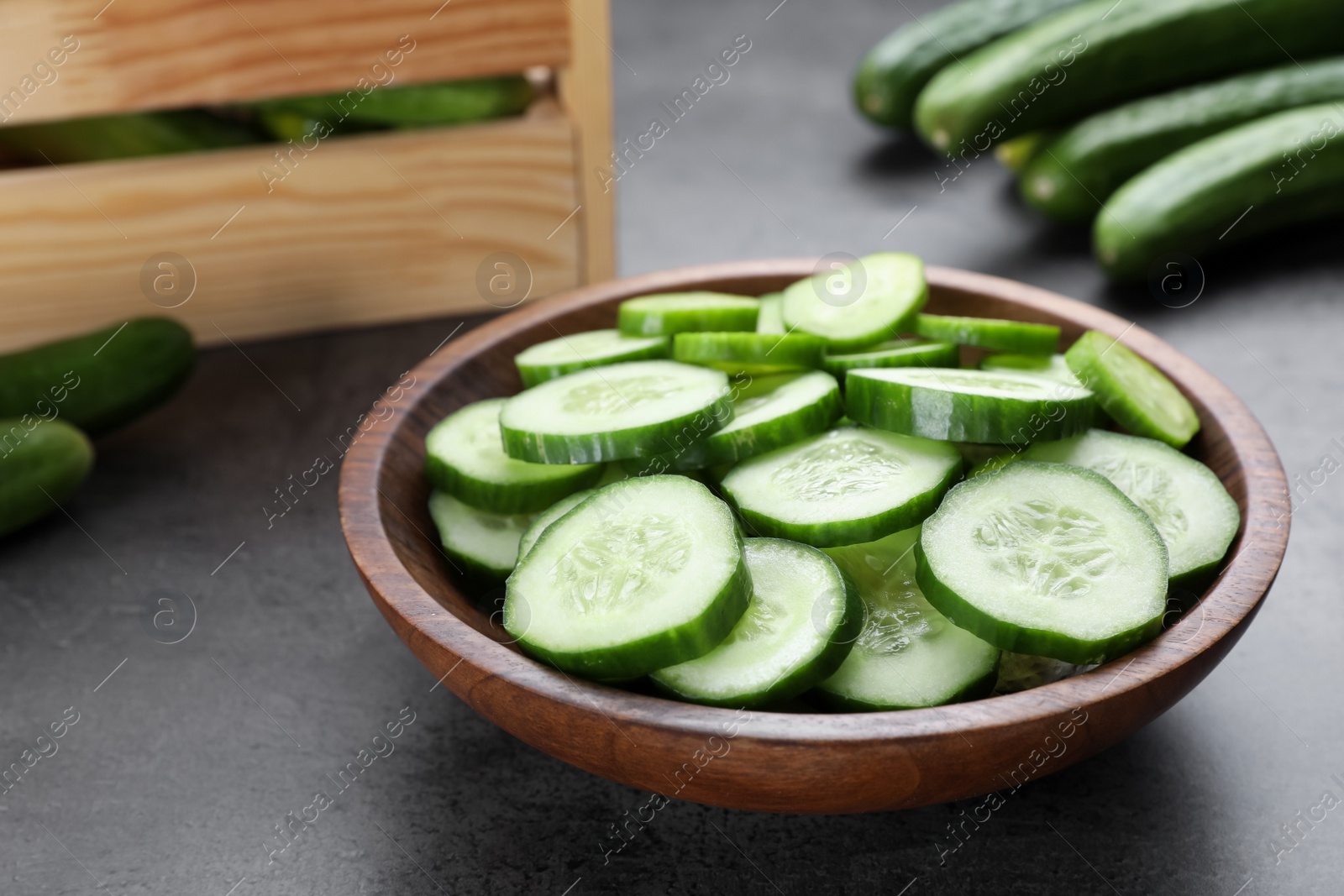 Photo of Slices of fresh ripe cucumber in bowl on grey table, closeup