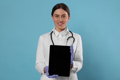 Photo of Doctor with stethoscope holding blank tablet on light blue background, space for design. Cardiology concept