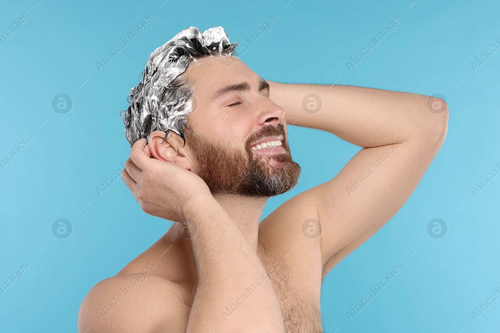 Photo of Happy man washing his hair with shampoo on light blue background, closeup