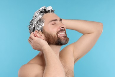 Happy man washing his hair with shampoo on light blue background, closeup