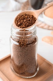 Photo of Spoon of instant coffee over jar on white table