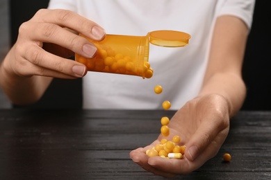 Photo of Woman pouring pills out of bottle into hand at table, closeup