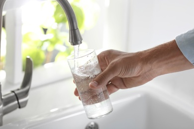 Photo of Man pouring water into glass in kitchen, closeup