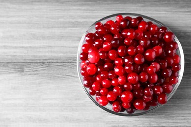 Photo of Fresh ripe cranberries in bowl on grey wooden table, top view. Space for text