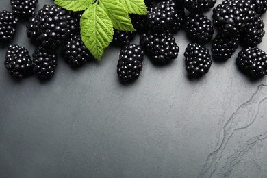 Photo of Tasty ripe blackberries with leaves on slate plate, flat lay. Space for text